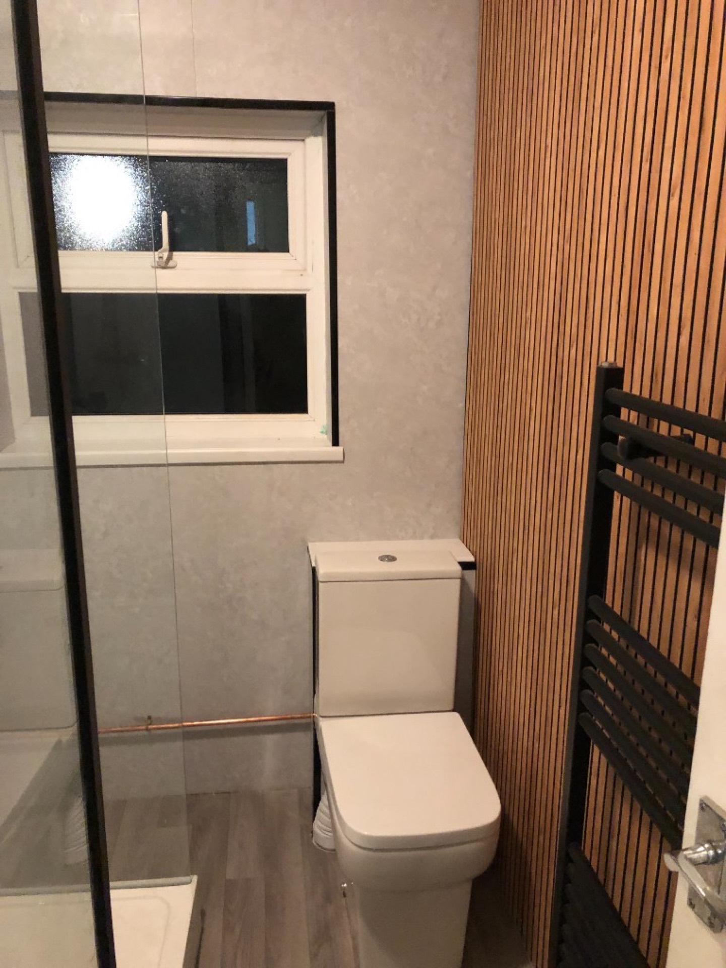 Finished compact bathroom with wood-slat feature wall, matte black heated towel rail and white WC